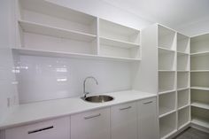 a kitchen with white cupboards and a sink in the center, next to an open shelving unit