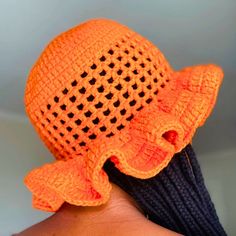 an orange crocheted hat with black dots on the brim is held up by a woman's hand