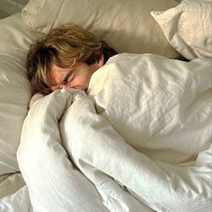 a man sleeping in bed with white sheets