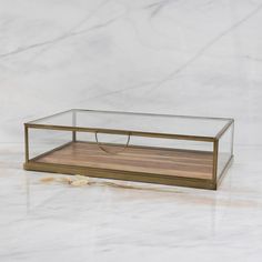 a glass and wood box sitting on top of a white marble counter with a wooden tray underneath it