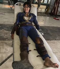 a woman sitting on top of a white bed next to a giant pair of boots