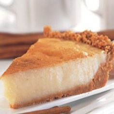 a slice of cheesecake on a white plate with cinnamon sticks next to it and a cup of coffee in the background