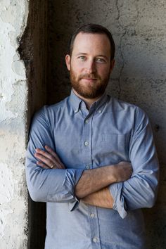 a man with his arms crossed standing in front of a wall and looking at the camera