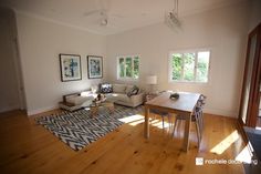 a living room filled with furniture next to a wooden table and two windows on top of a hard wood floor