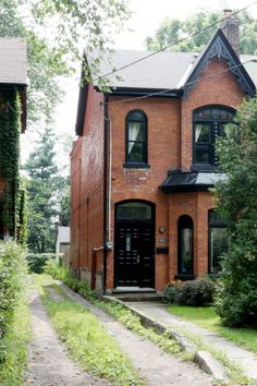 an old brick house with black trim on the front and side windows, surrounded by greenery