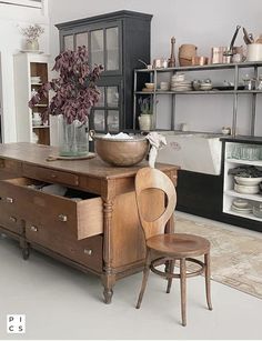 an old fashioned kitchen with wooden furniture and pots on the stove top, in front of shelves filled with dishes