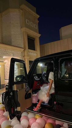 a woman sitting in the driver's seat of a black car next to balloons