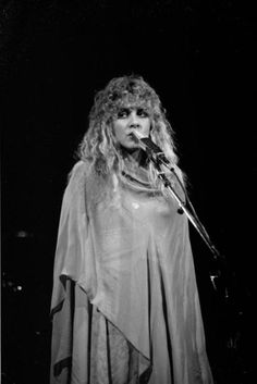 a woman with long hair standing in front of a microphone and wearing a cape on her head