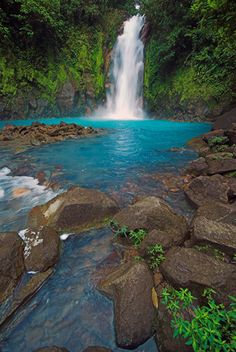 a waterfall with blue water surrounded by rocks and greenery