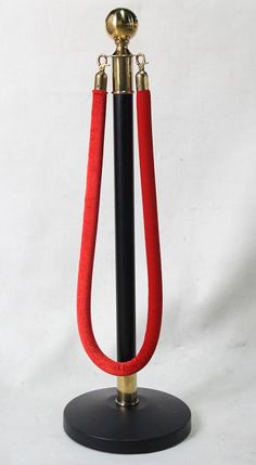 a red and black object on a stand with a gold top, metal base and two handles