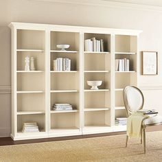 a white bookcase with many books on it and a chair in the corner next to it