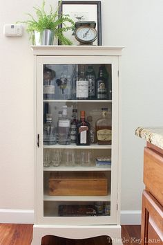 a white cabinet filled with liquor bottles and glasses on top of a hard wood floor