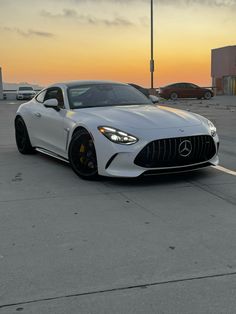 a white mercedes sports car parked in a parking lot at sunset with other cars behind it