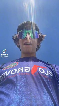 a man with goggles on standing in front of blue sky and sun shining through the lens