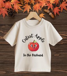 Your little one will look super cute in this "Cutest Apple in the Orchard" t-shirt! With a happy red apple and fun text, this tee is perfect for fall outings or apple-picking adventures. It's soft and comfy, great for all-day wear. Let your kiddo be the cutest apple in the orchard. Made from soft, comfy fabric, it's perfect for the fall season. Uplift any child's wardrobe with a custom kid's t-shirt. The Bella Canvas short sleeve tee for toddlers is a 100% Airlume combed and ring-spun cotton jer Toddler Apple Picking Outfit, Playful Short Sleeve T-shirt For Fall, Cute Slogan T-shirt For Gift, Cute Fall T-shirt For Gift, Cute Slogan T-shirt For Gifts, Playful Short Sleeve Fall T-shirt, Cute T-shirt With Funny Text As Gift, Cute Slogan T-shirt For Fall, Cute Fall T-shirt With Slogan