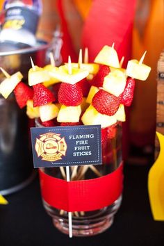 strawberries and apples are arranged on sticks in a clear glass vase with a fireman's name tag