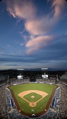 an aerial view of a baseball field at dusk with clouds in the sky above it