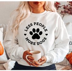 a woman is holding a coffee cup and wearing a sweatshirt with the words less people more dogs on it