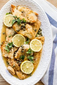 a white plate topped with chicken covered in lemons and capers on top of a wooden table