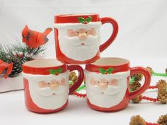 four mugs with santa claus on them and pine cones in the foreground, along with other christmas decorations