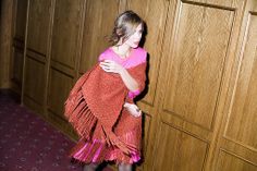 a woman standing in front of a wooden wall holding a red and pink shawl