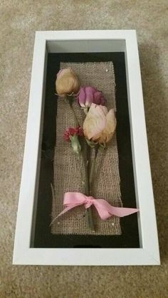 three dried flowers in a white frame with pink ribbon tied around them on the floor