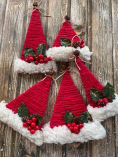 three crocheted christmas hats with holly berries and pine cones hanging from the top