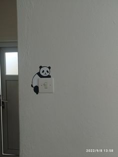 a black and white panda bear sticker on the wall next to a light switch