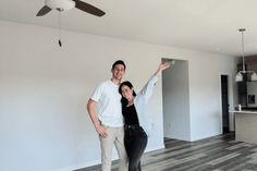 a man and woman standing in an empty living room with ceiling fan on the wall