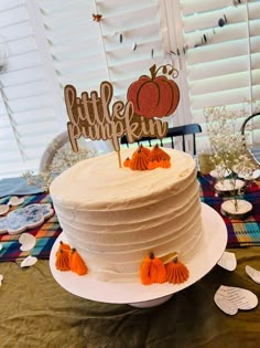 a white cake sitting on top of a table next to a sign that says little pumpkin