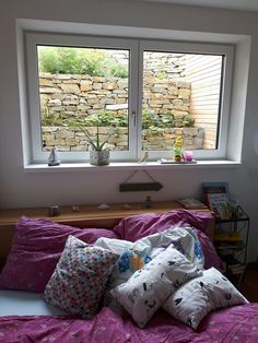 a bed with four pillows on it in front of two large windows that look out onto the garden