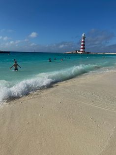 people swimming in the ocean near a lighthouse