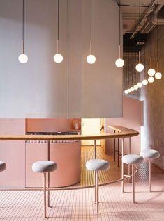 an office with pink walls and white stools in front of a round wooden table