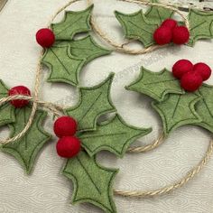 two felt holly wreaths with red berries hanging from twine on top of each other