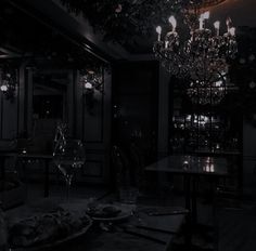 a chandelier hanging from the ceiling in a dark room with tables and chairs