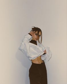 a woman in black pants and white shirt posing for the camera with her hands on her head