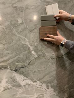 a person is holding some kind of book on a marble surface with wood and metal accents