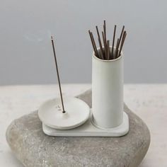 a white cup with sticks sticking out of it sitting on top of a stone slab