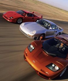 three different colored sports cars driving on a track