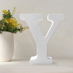 a white vase with yellow flowers in it next to a letter shaped like the letter y