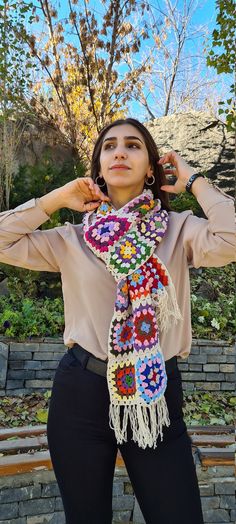 a woman poses with her hands on her hips wearing a multicolored crocheted scarf