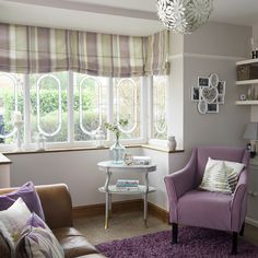 a purple chair sitting in front of a window next to a table with a vase on it