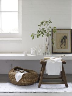 a white bath room with a wooden stool and potted plant on the shelf next to it