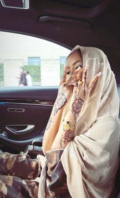 a woman sitting in the back seat of a car talking on a cell phone and covering her face with a shawl