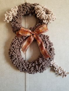 a knitted wreath hanging on the side of a door with a plaid bow around it