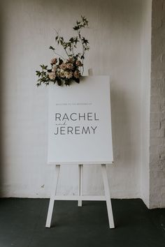 a sign with flowers on it in front of a white wall that says rachel jeremy