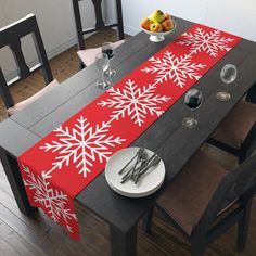 a dining room table with red and white snowflakes on the table runner next to silverware