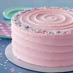 a pink frosted cake with sprinkles sits on a plate next to confetti