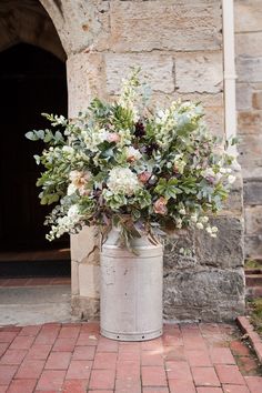 a bunch of flowers that are in a bucket on the ground by some bricks and a door