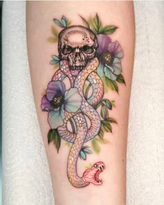 a skull and snake tattoo on the leg, with flowers around it's ankles